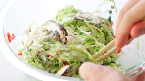 Mixing Okonomiyaki batter together in a glass bowl with chopsticks.