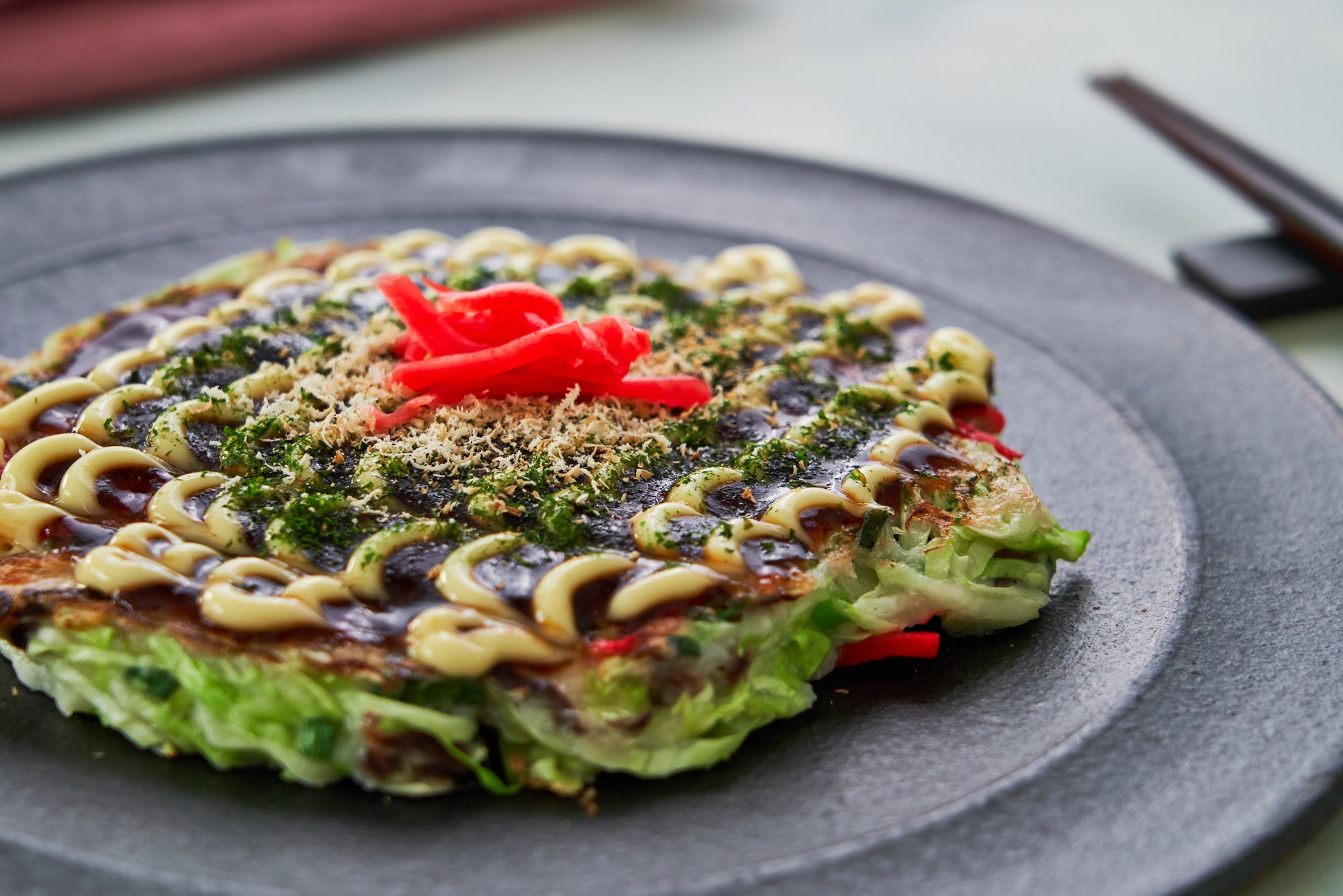 Vegan Okonomiyaki slathered in okonomiyaki sauce, plant-based mayonnaise, aonori, and dried shiitake mushroom flakes.