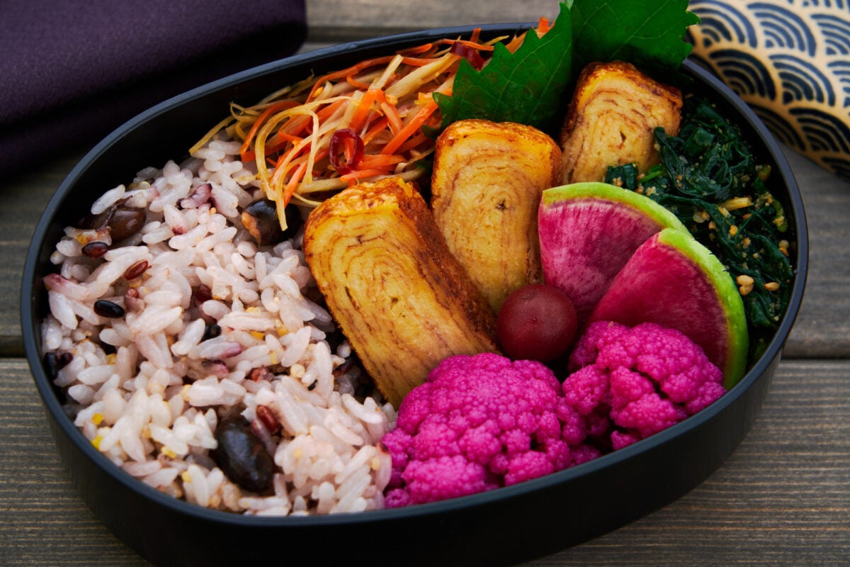 Japanese bento box lunch with vegan tamagoyaki, pickled cauliflower, sesame spinach, and stir-fried burdock with carrots.