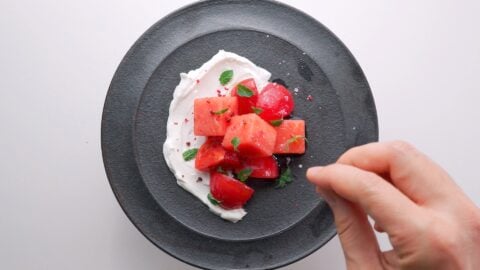 Sprinkling sea salt on a watermelon and tomato salad.