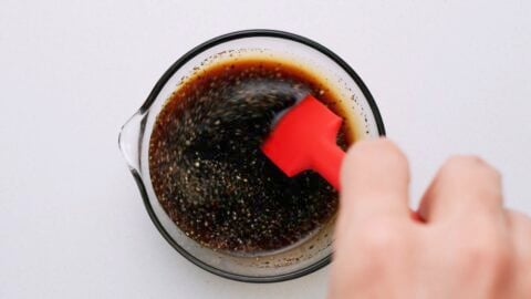 Stirring Yaki Udon sauce with a red spatula in a glass bowl.