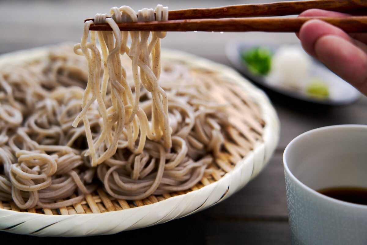 Chilled soba noodles get lifted off a zaru with chopsticks for dipping into soba sauce.