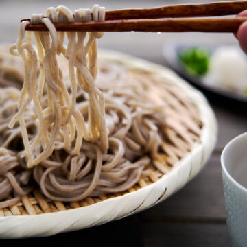 Chilled soba noodles get lifted off a zaru with chopsticks for dipping into soba sauce.