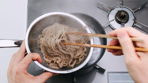 Transferring the cooked soba from the pot to a strainer.